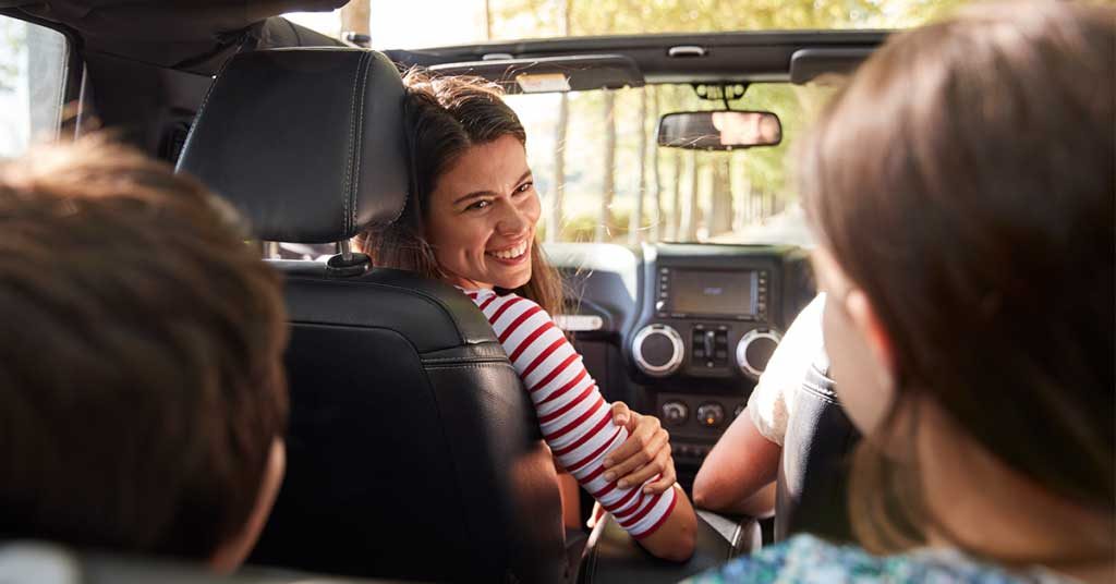 Mom smiling as she looks back at kids from front seat of car