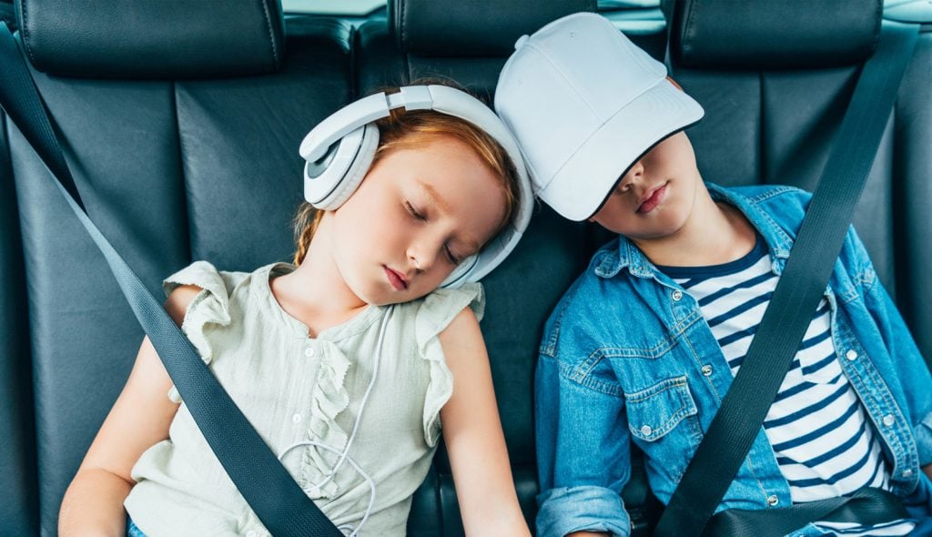 Two children buckled, but asleep on the back seat of a car.