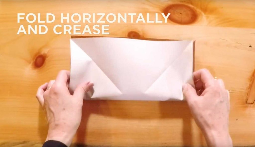 Paper being folded in half with text that says, "Fold horizontally and crease."