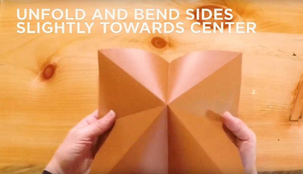Paper being unfolded with text that says, "Unfold and bend sides slightly towards center."