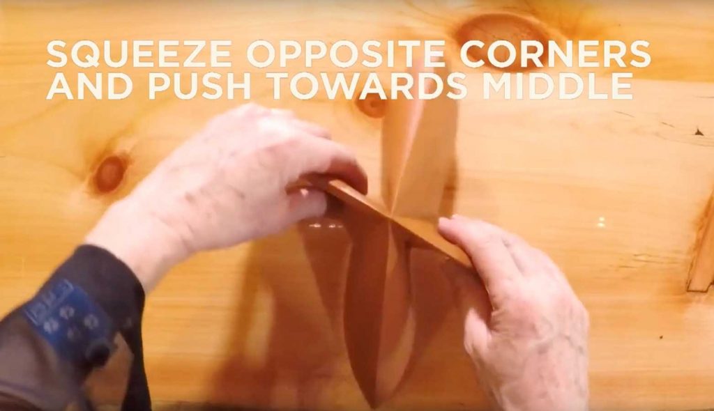 Paper being folded in fourths with text that says, "Squeeze opposite corners and push towards middle."