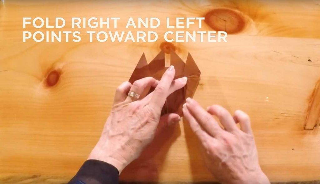Paper being folded with text that says, "Fold right and left points toward center."