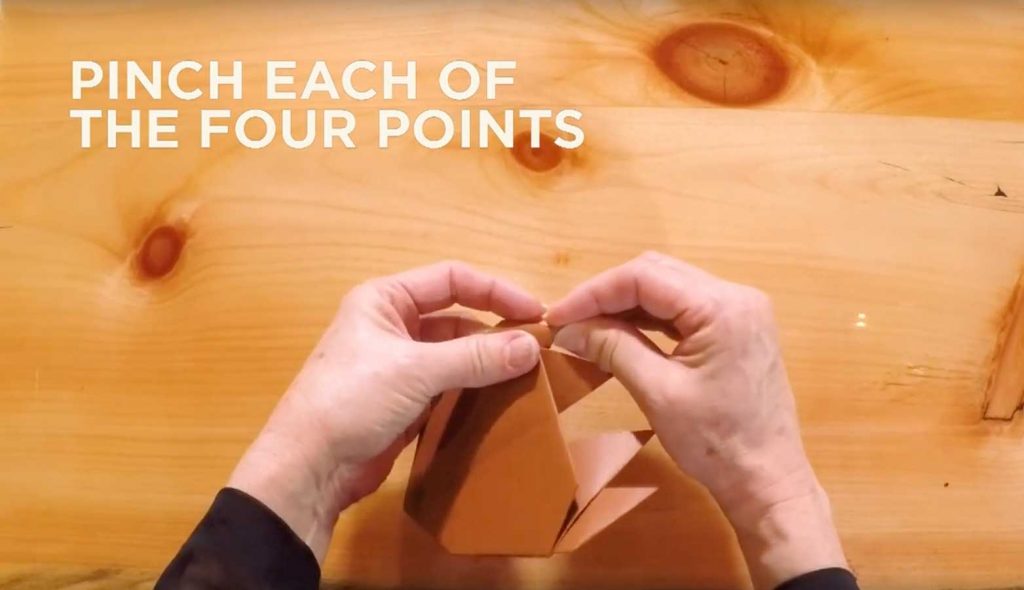 Paper being folded with text that says, "Pinch each of the four points."
