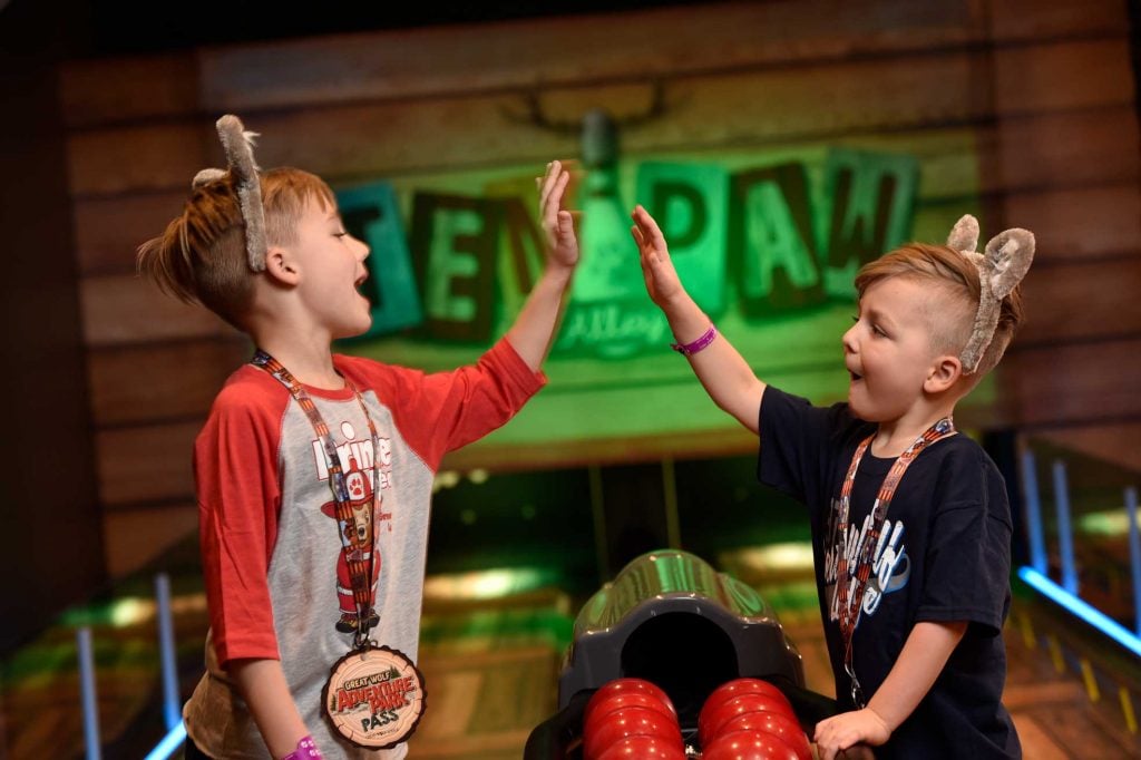 2 children high-fiving each other at the Ten Paw Alley bowling lanes at a Great Wolf Resort.