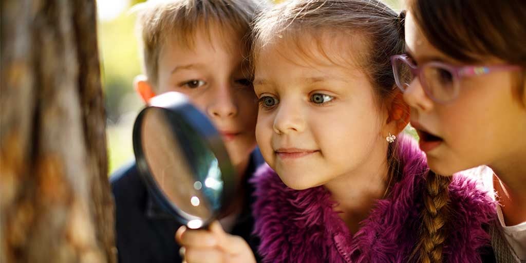 Three kids looking at a tree with a magnifying glass