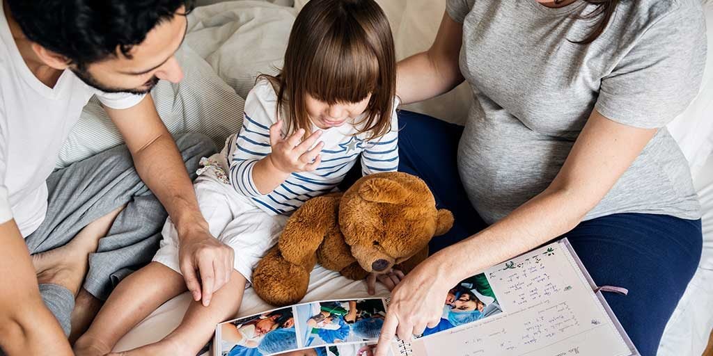 Pregant mom and dad show photo album to little girl