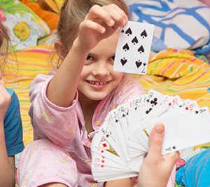 Child picking a 7 of spades card from a fanned out deck being held by another person.