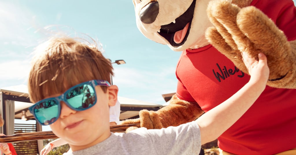 Young boy in sunglasses high-fives Wiley Wolf at Great Wolf Lodge.