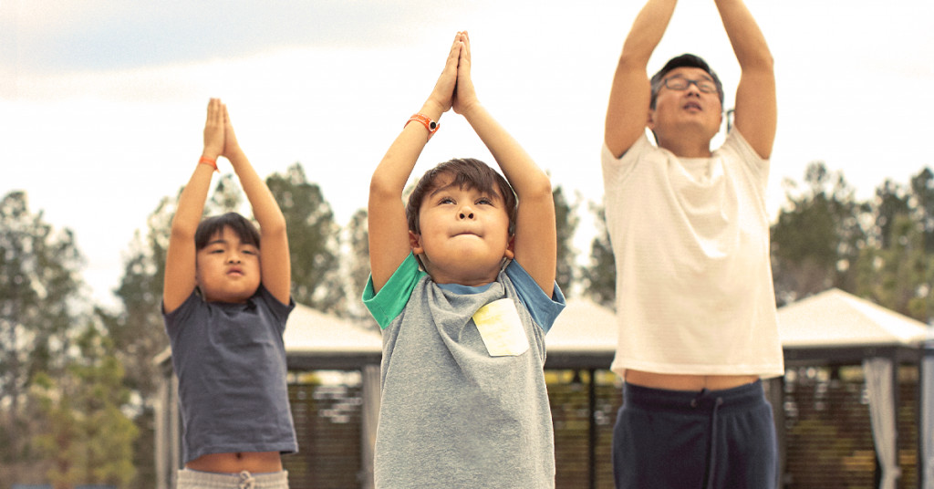 Father and two sons do outdoor yoga.