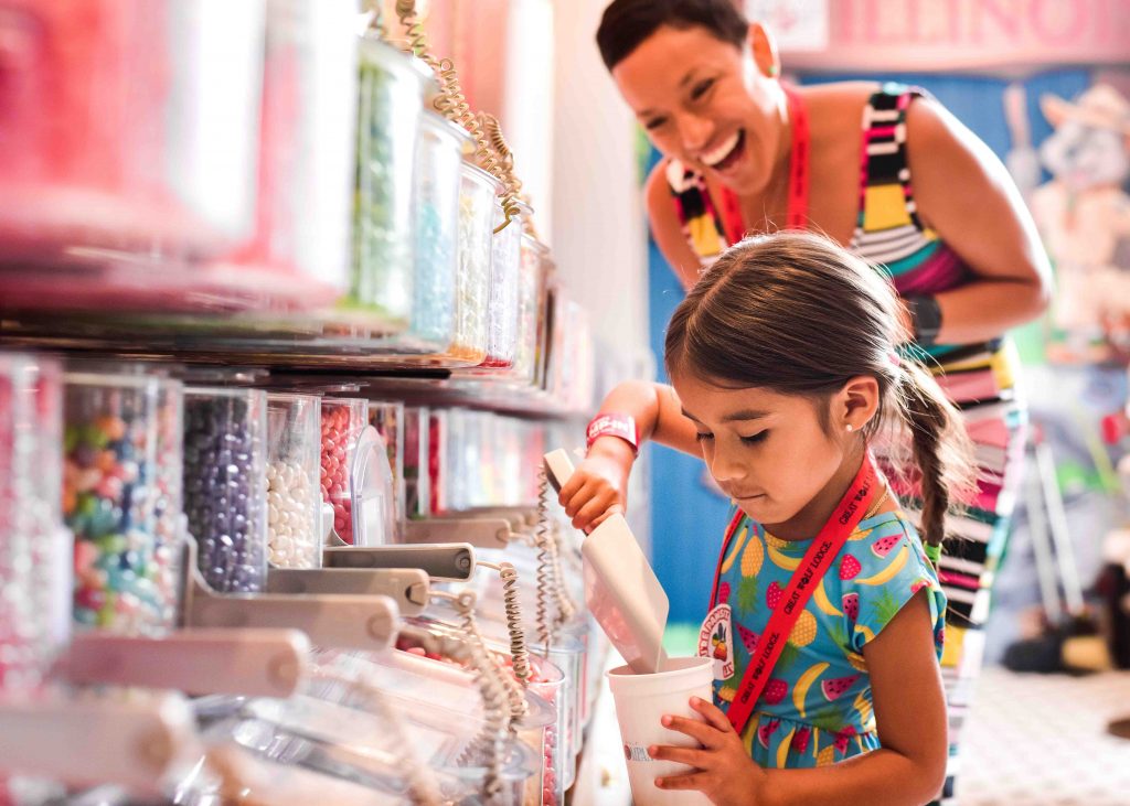 Mom smiling at girl as she scoops candy inside Great Wolf Resorts Candy Company. 