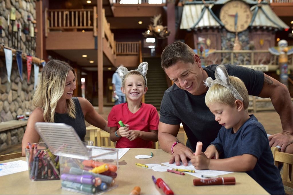 Family with mom, dad and two boys in the lobby of Great Wolf Lodge doing crafts around a table.