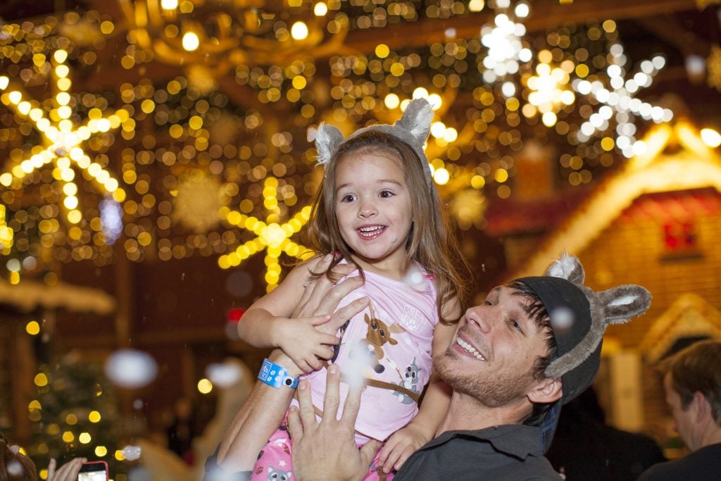 Little girl on dad's shoulder as snow falls inside Great Wolf Lodge's decorated lobby.