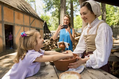 A woman photographs her child interacting with a performer at the Jamestown Settlement and American Revolution Museum