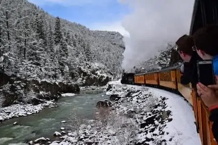 Passengers enjoy a view of snow-covered Rocky Mountains aboard the Narrow Gauge Railroad
