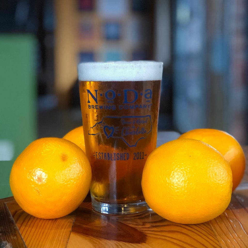 A tall beer surrounded by lemons on a wooden table at the Noda Brewing Company