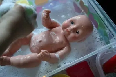 Washing a doll in the sink with soap and water