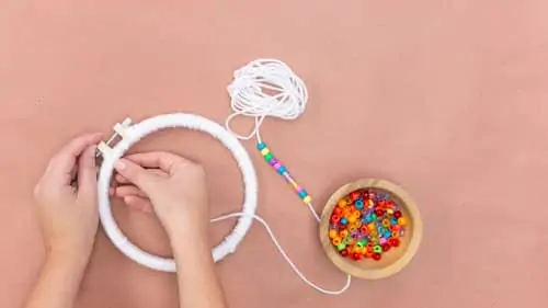 embroidery hoop covered in white yarn and bowl of covered beads