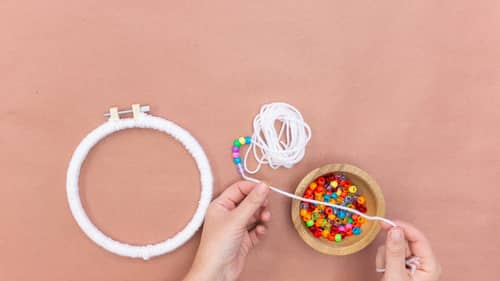 embroidery hoop covered in white yarn and colored beads