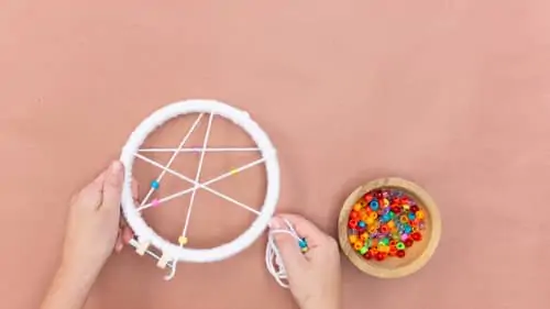 Cross the yarn string of plastic beads across the embroidery hoop