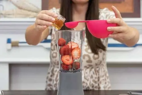 woman adding honey to blender with strawberries