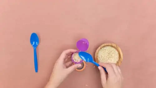 pouring rice into purple plastic egg using blue plastic spoon