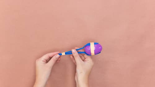 wrape blue plastic spoons to purple plastic egg using orange decorative tape. tape spoons together at ends using orange decorative tape