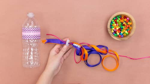 Thread the blue and orange embroidery floss and ribbon into the hole in the plastic water bottle top