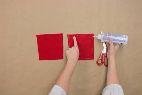 woman cutting out two red squares of red felt and gluing onto cardboard