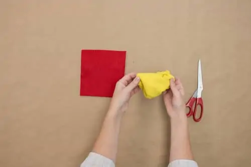 woman cutting out a square of yellow felt and gluing onto cardboard