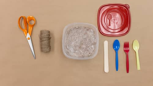 scissor, twine, plaster mixture, red tupperware, stick, blue spoon, red fork, yellow spoon