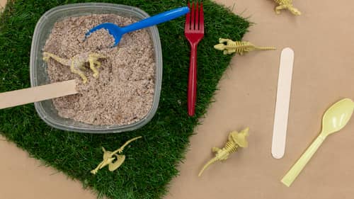 popsicle sticks and plastic spoons to excavate dinosaur figurines in kids diy activity