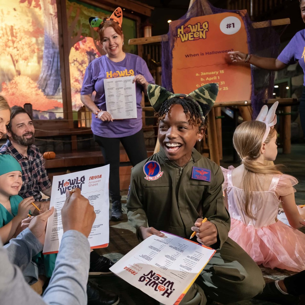 Families in Halloween costumes laugh while playing Howl-O-Ween trivia with Great Wolf Lodge staff.