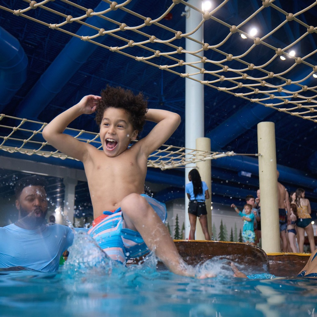 Boy jumps in the water pool as his parents look at him feeling happy