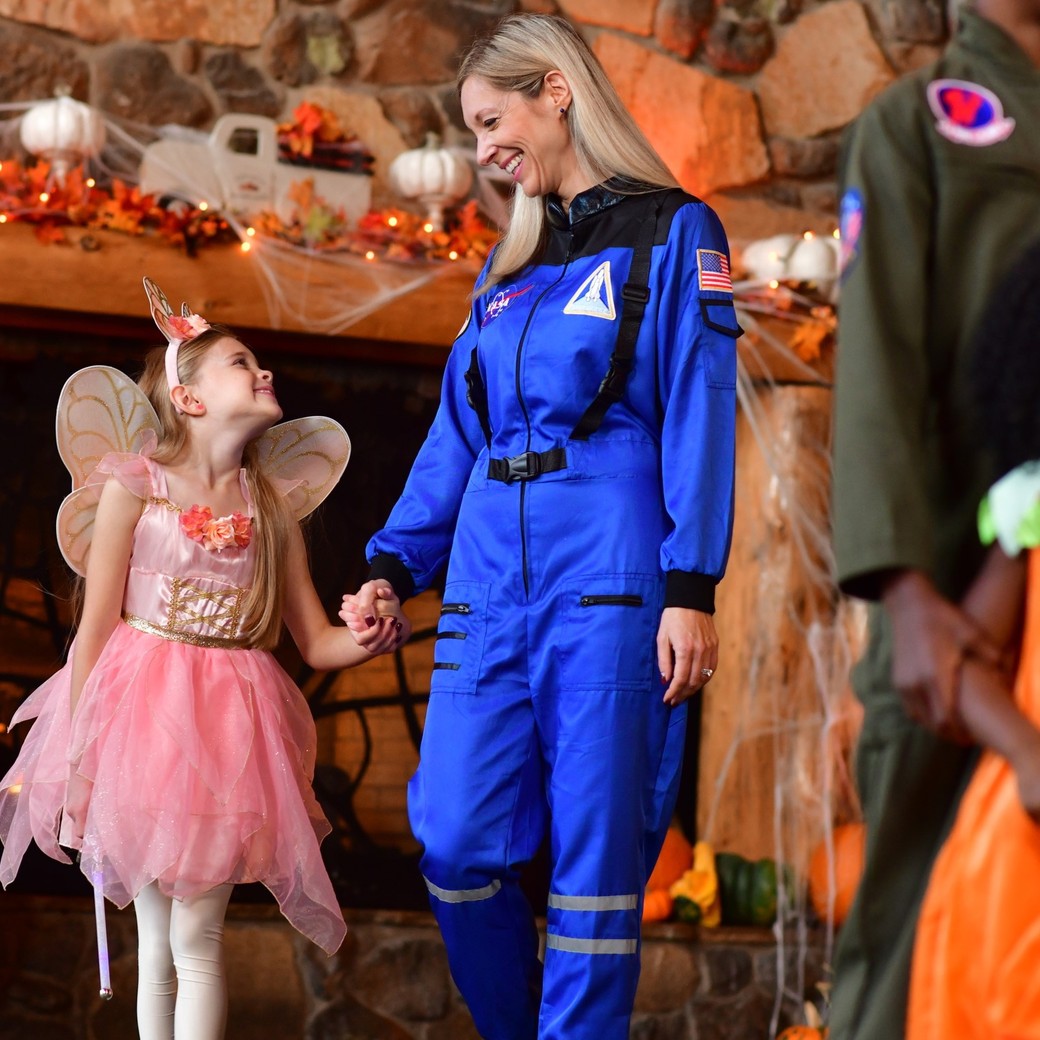 Child in fairy costume meeting astronaut character indoors.