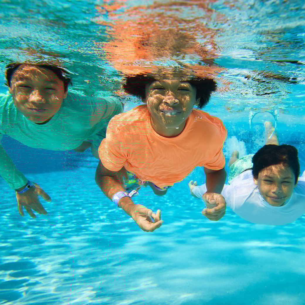 three children smiling underwater in a swimming pool