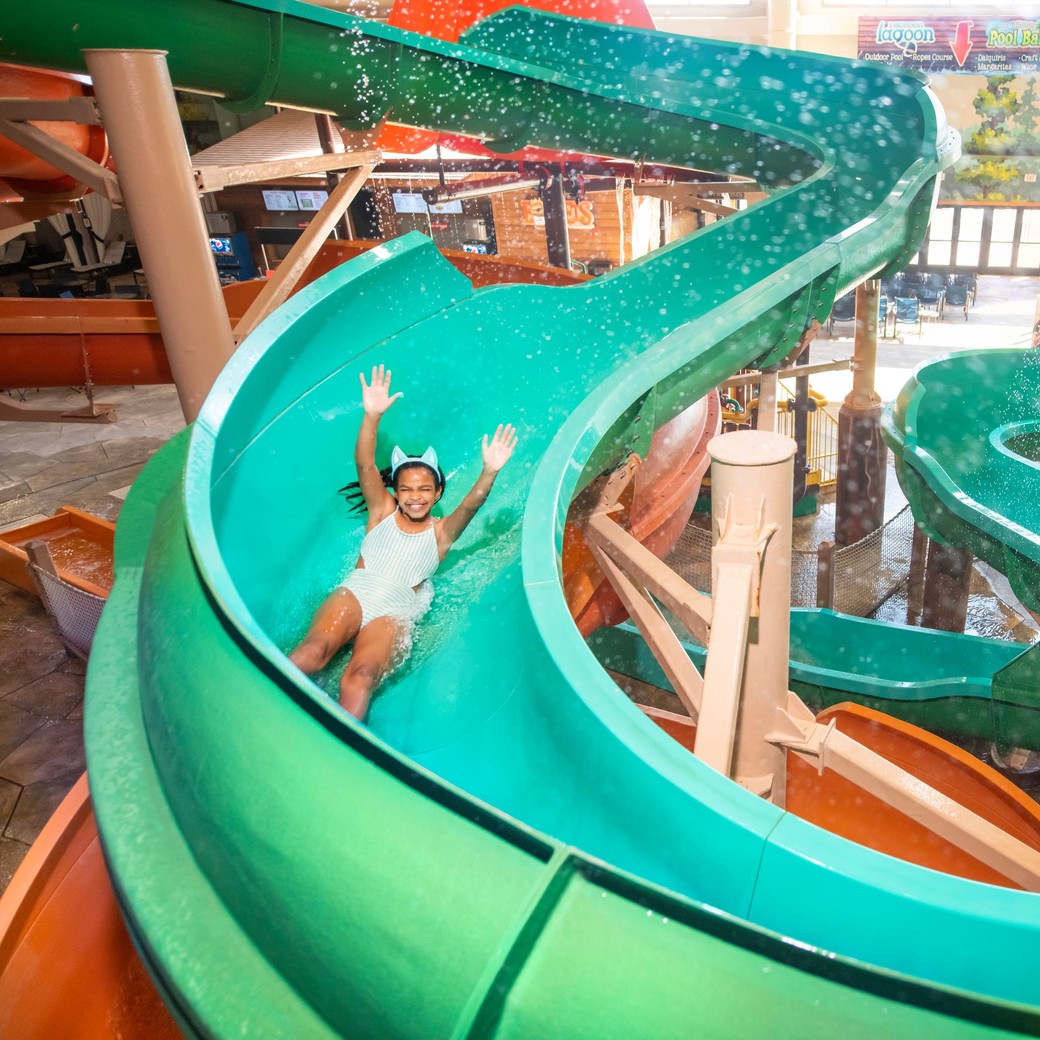 Child sliding down bright turquoise water slide with hands raised.