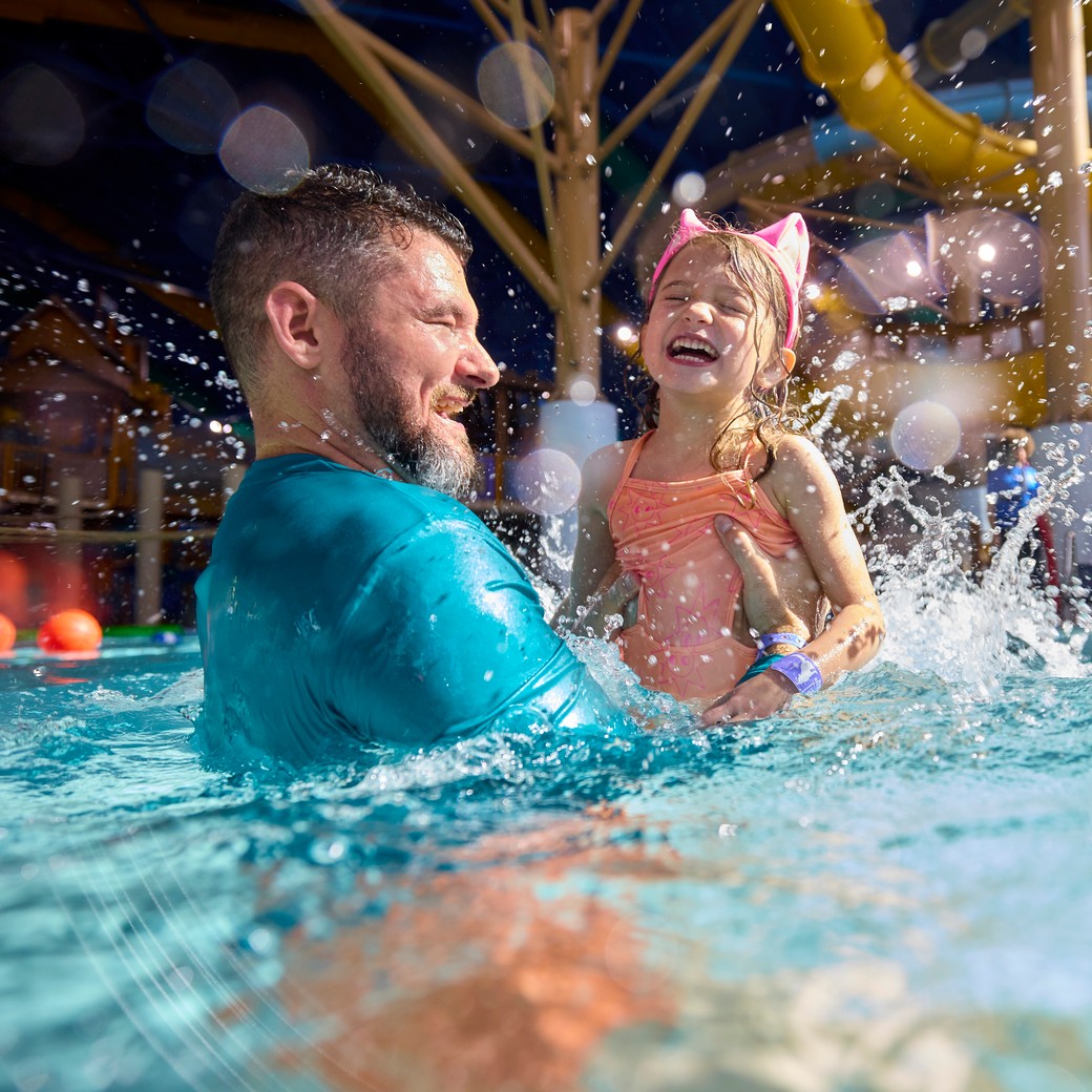 Smiling father and daughter laughing and splashing in a water park pool