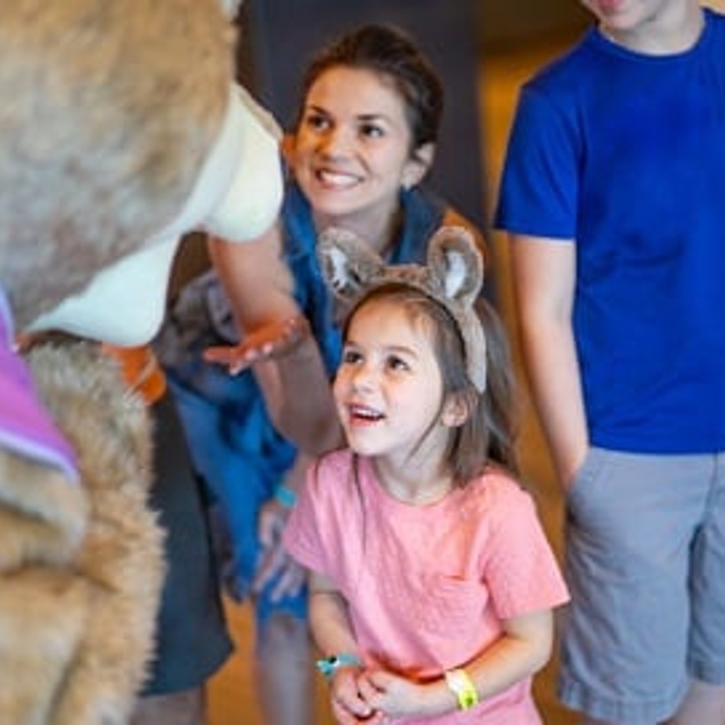 A girl wearing wolf ears looks up at a Great Wolf Lodge character.