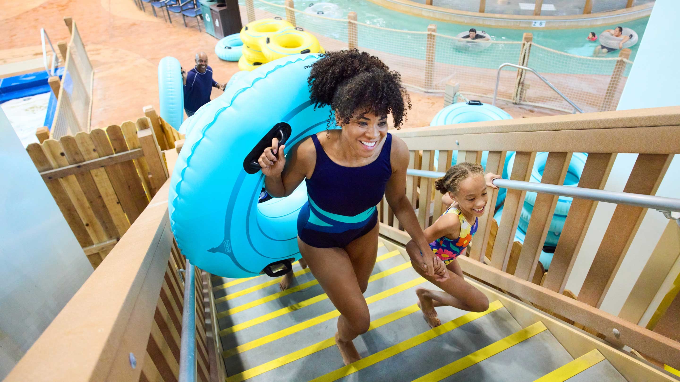 mother and daughter climbing up stairs holding a tube to slide down a water ride