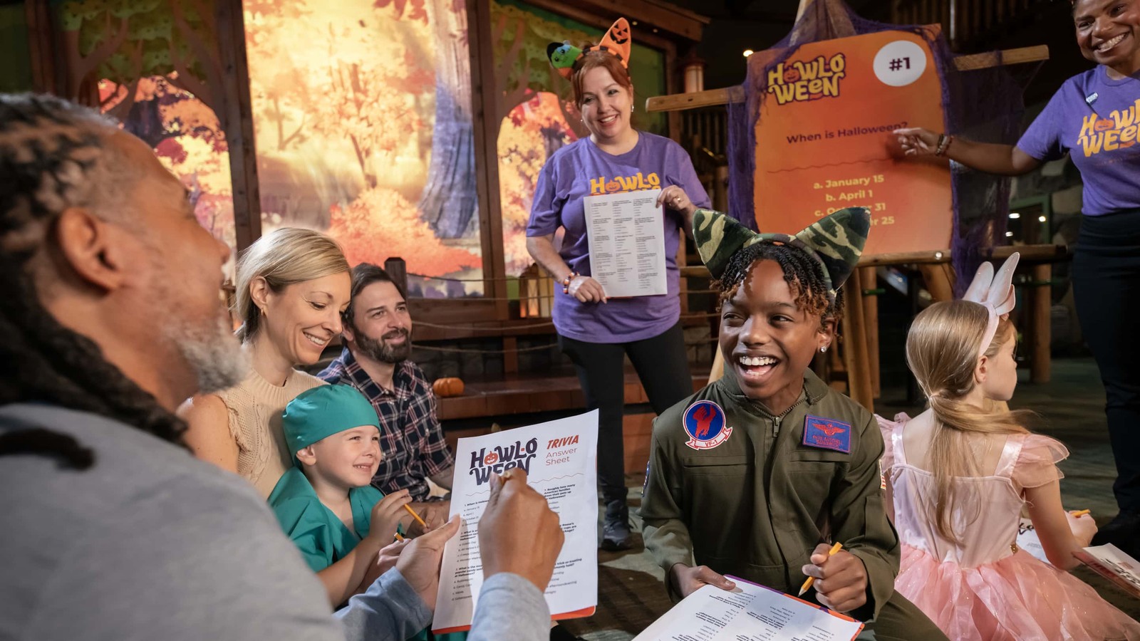 Families in Halloween costumes laugh while playing Howl-O-Ween trivia with Great Wolf Lodge staff