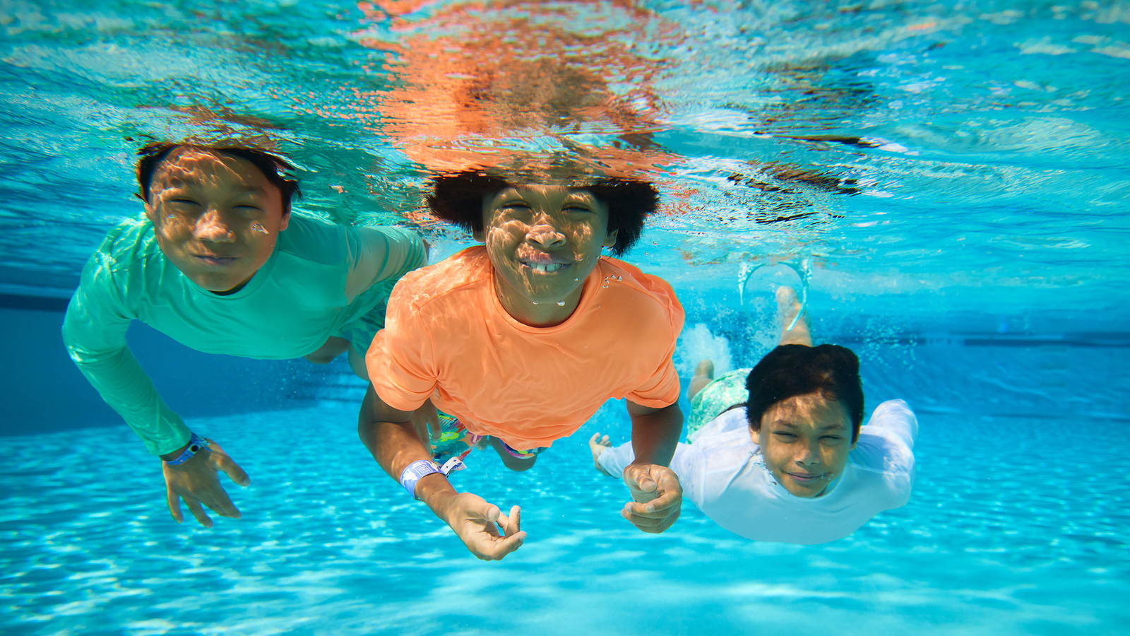 Three children smiling underwater in a swimming pool