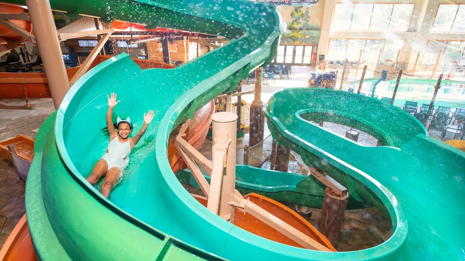 Child sliding down bright turquoise water slide with hands raised.