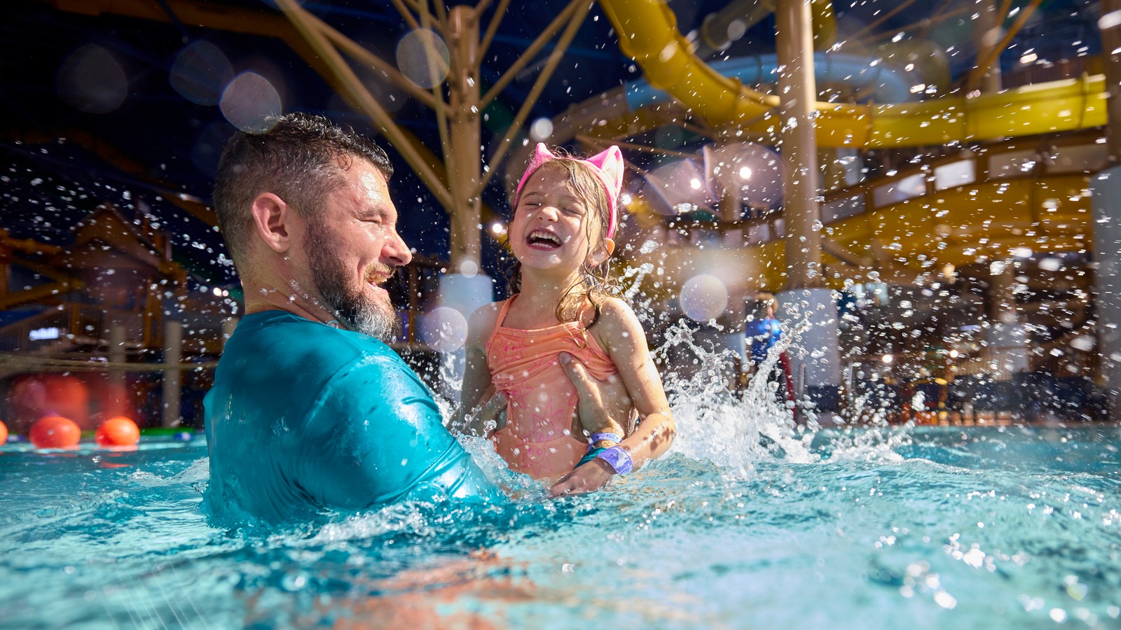 Smiling father and daughter laughing and splashing in a water park pool