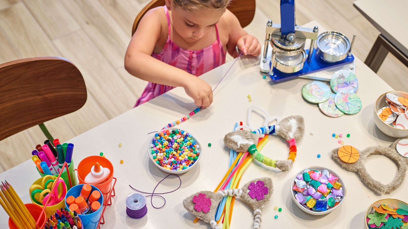 Young girl crafting with beads and supplies at a table.
