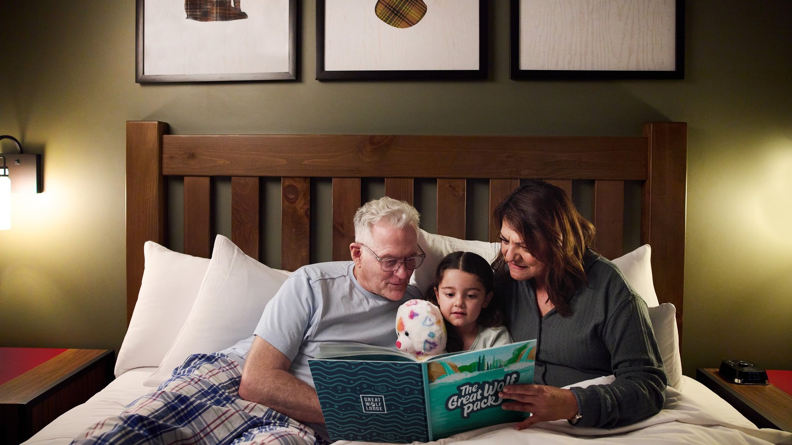 grand parents sitting in a hotel bed along with there grand child reading a story book