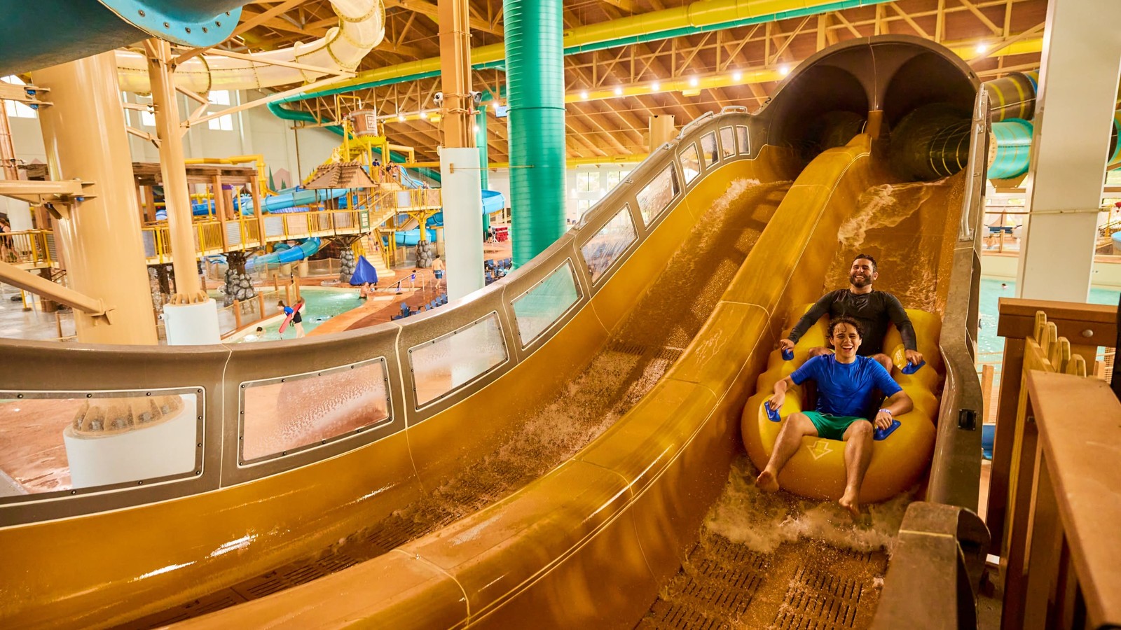 Two family members rides down waterslide on yellow tube 