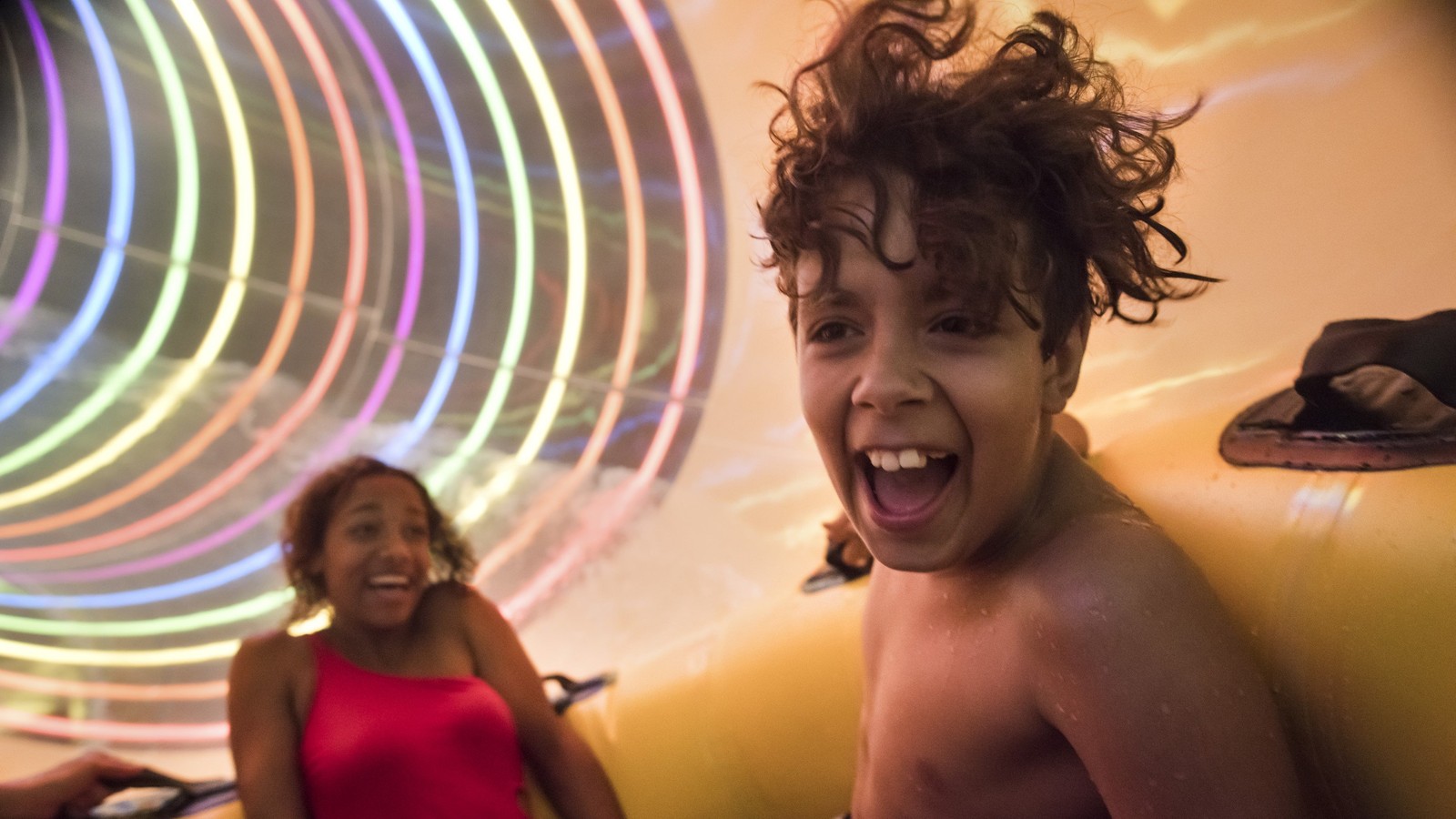 Two kids in yellow raft going fast down a colorful waterslide