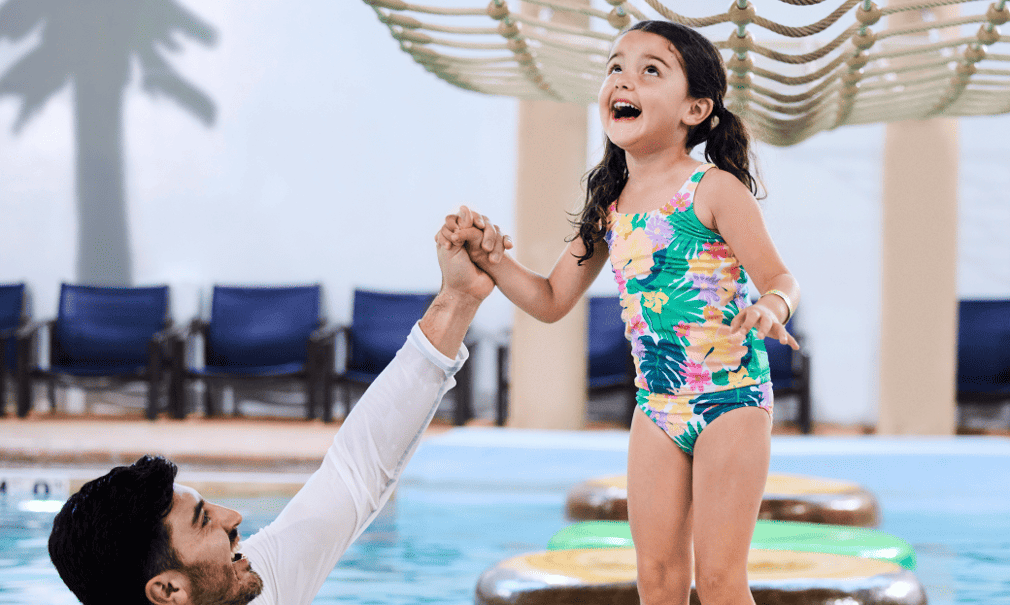 A girl balances on a lily pad float in indoor pool