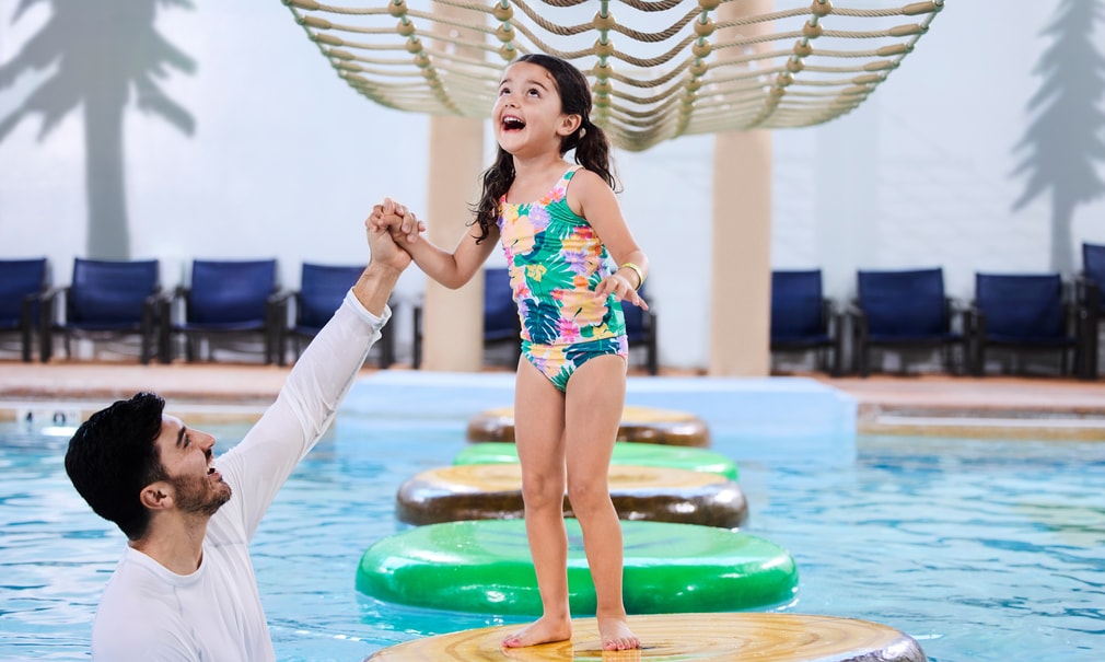A girl balances on a lily pad float in indoor pool