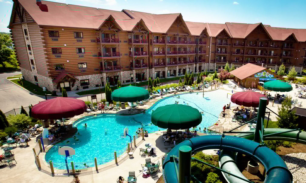 Aerial view of outdoor pool area featuring water slides, shaded seating under colorful umbrellas, and guests enjoying a sunny day.